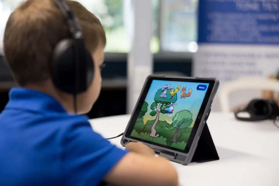 A child wearing headphones engages with the on-screen Sound Scouts characters during the hearing test on a tablet