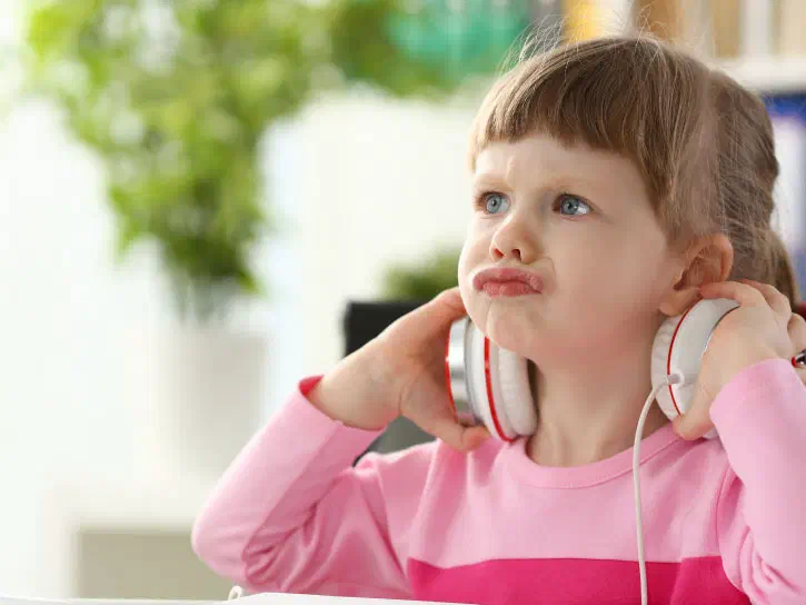 Young child frustratingly holding headphones around her neck.