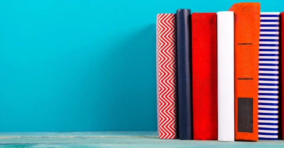 {{< i18n key="colourful" isFirstUpper=true >}} stack of books against a blue wall