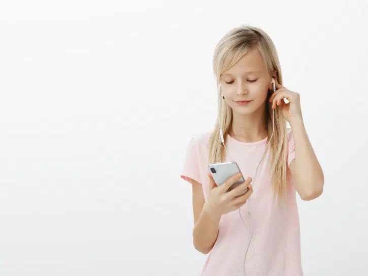 Young girl holding a mobile device connected to wired earbugs she places in her ears.