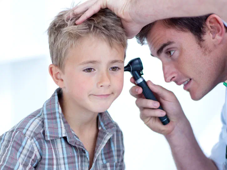 Young boy getting his ear checked by an adult using an otoscope.