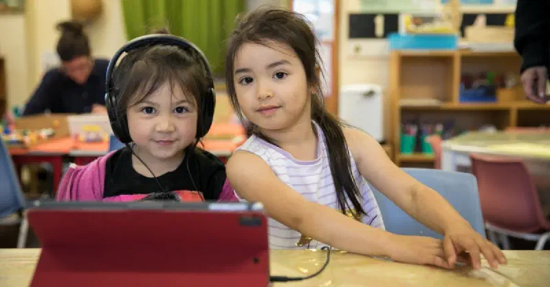 Two girls looking at camera, one with headphones on and tablet in front of her