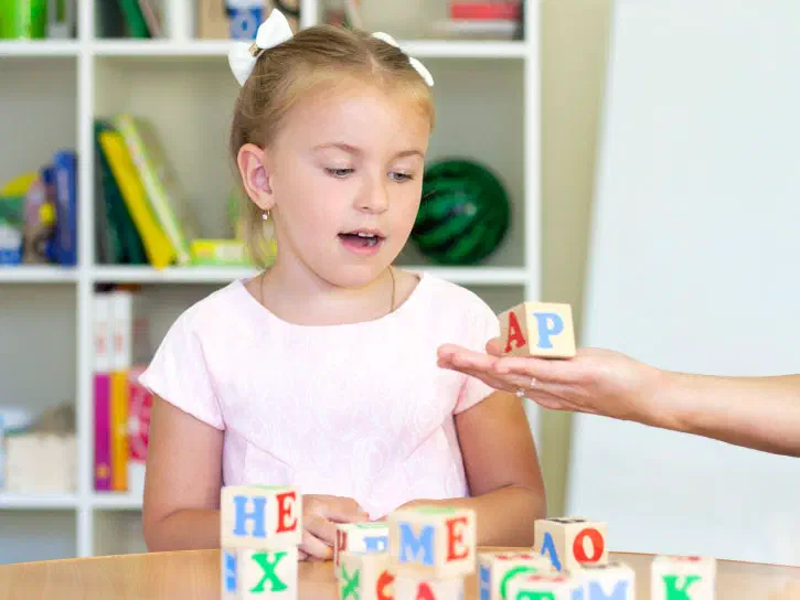 Child being shown a wooden phonics cube.