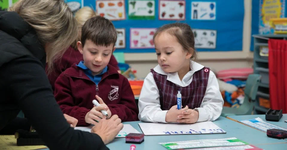 Two children in classroom listening to teacher instructions