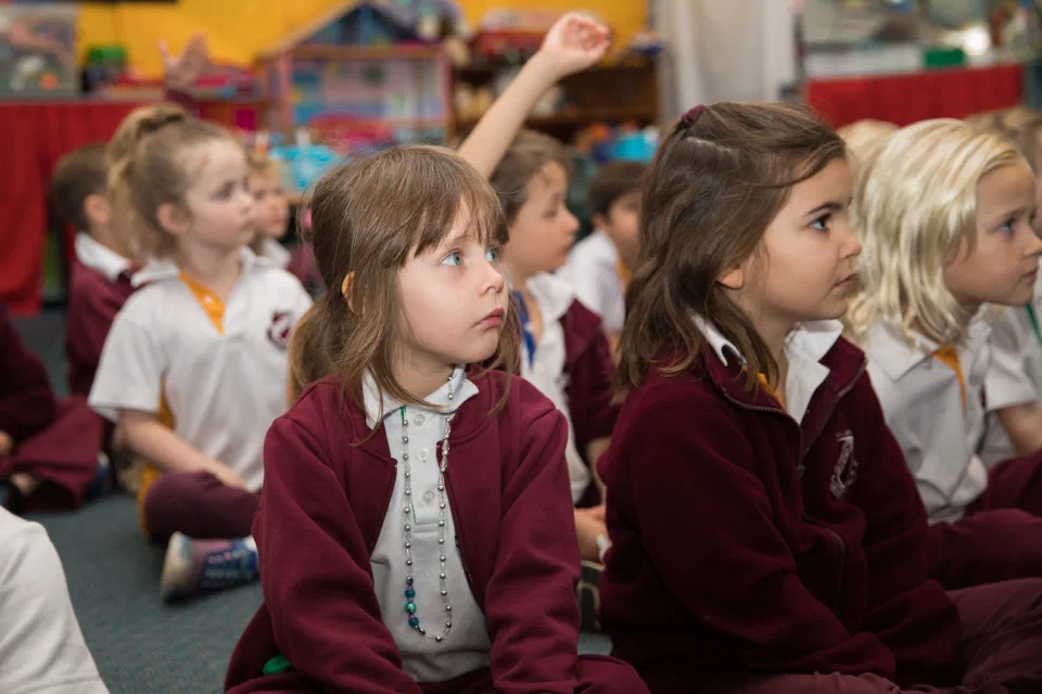 Group of young sitting on the floor of their classroom listening intently.